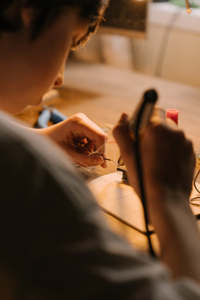 Young person intensely soldering a PCB, surrounded by tools, in a warm indoor setting.