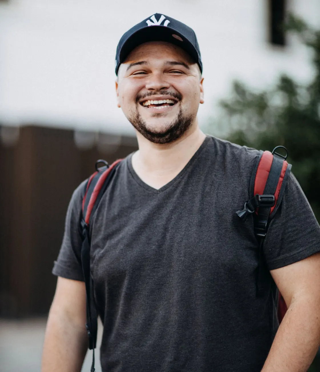 Happy man outdoors wearing a cap and backpack, smiling brightly.